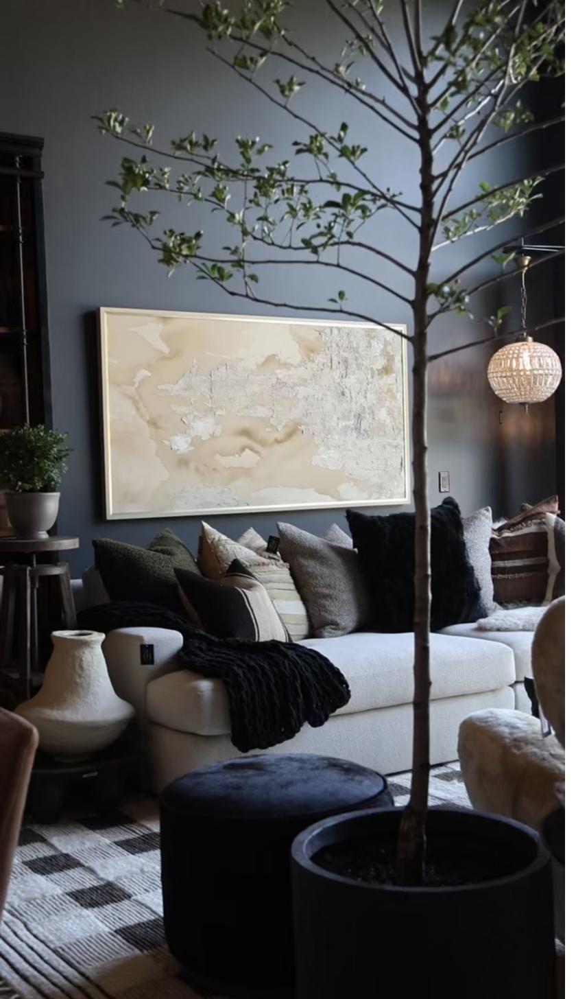 Large abstract textured painting in warm cream and gold tones with heavy impasto technique displayed above white sofa in dark moody living room