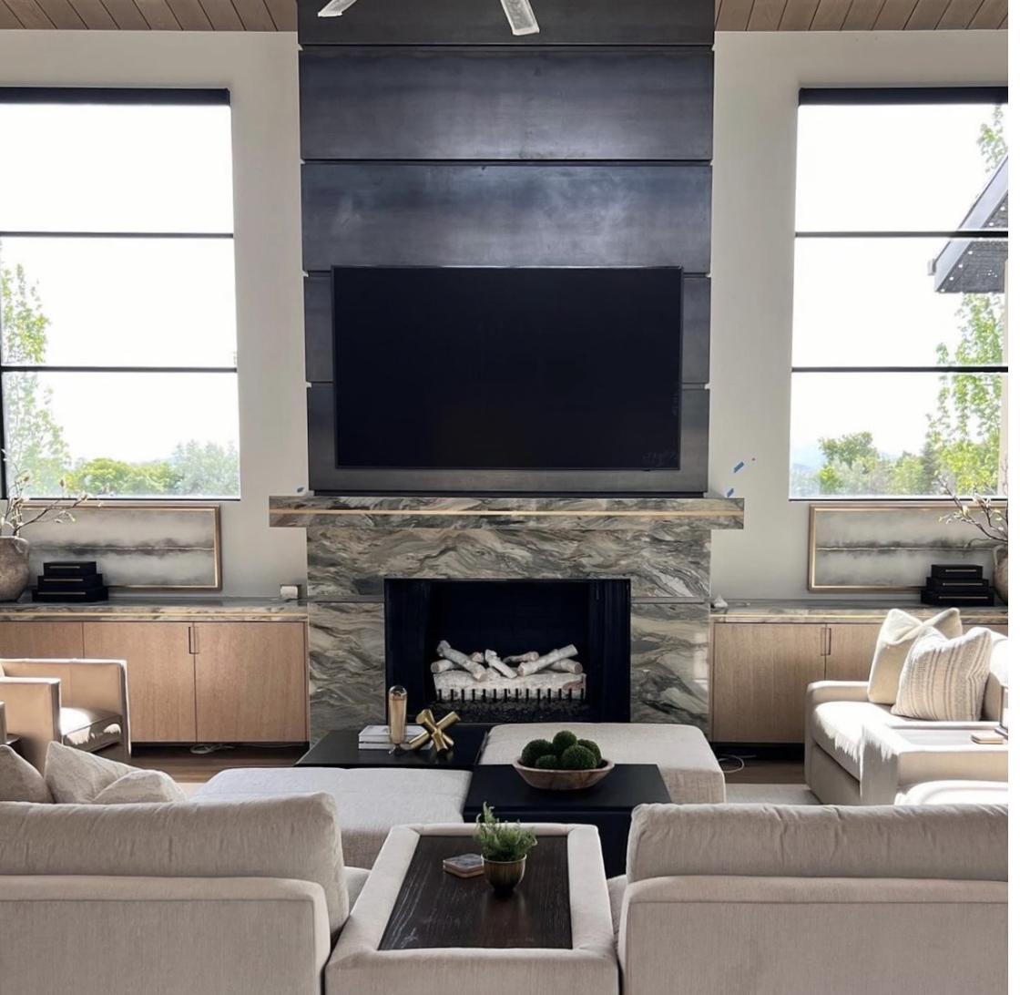 Pair of subtle abstract paintings in muted tones flanking modern stone fireplace with dark metal surround in contemporary living room with high ceilings