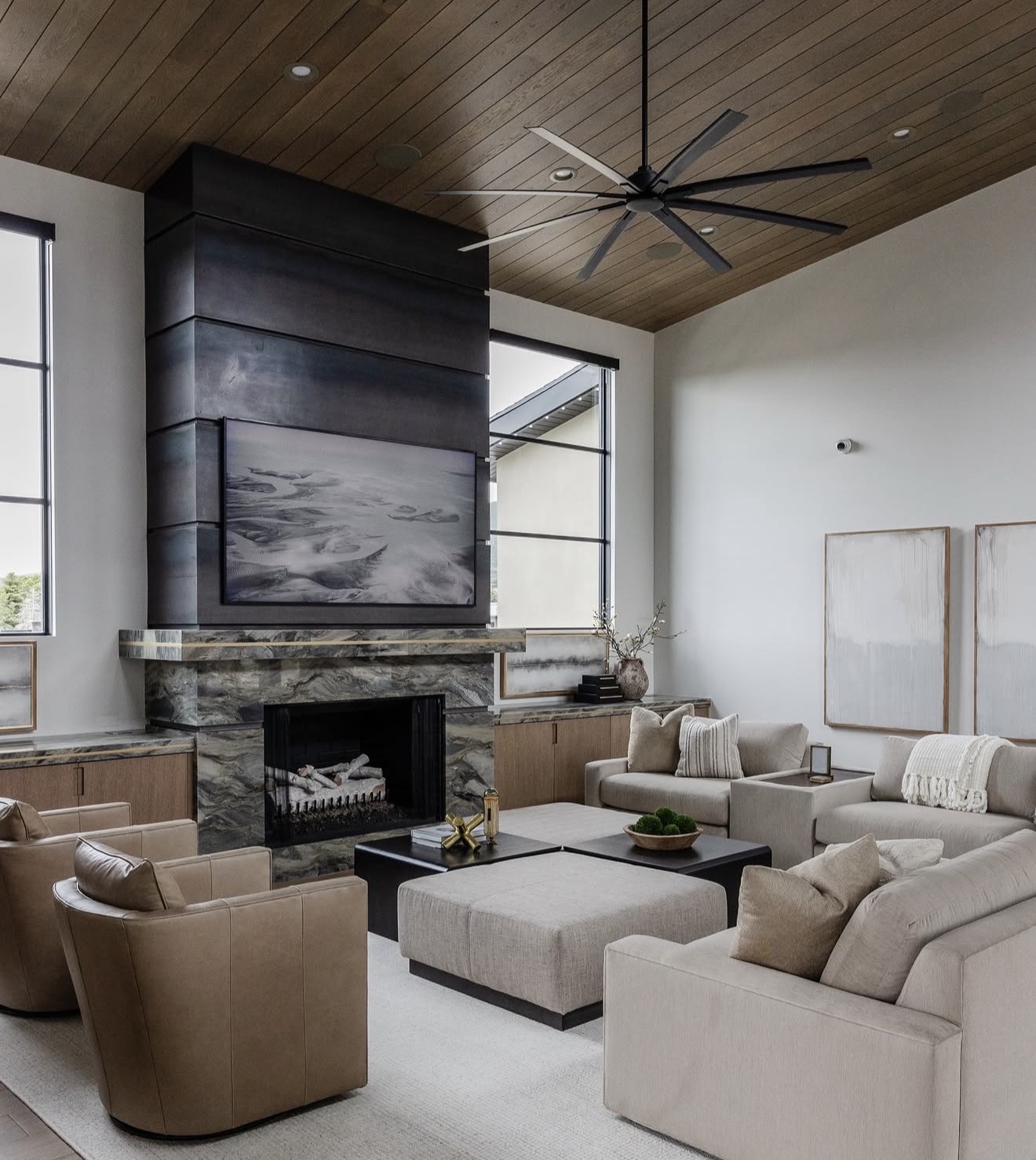 Multiple custom artworks displayed in expansive luxury living room with stone fireplace surround, vaulted wood ceiling, and contemporary furnishings