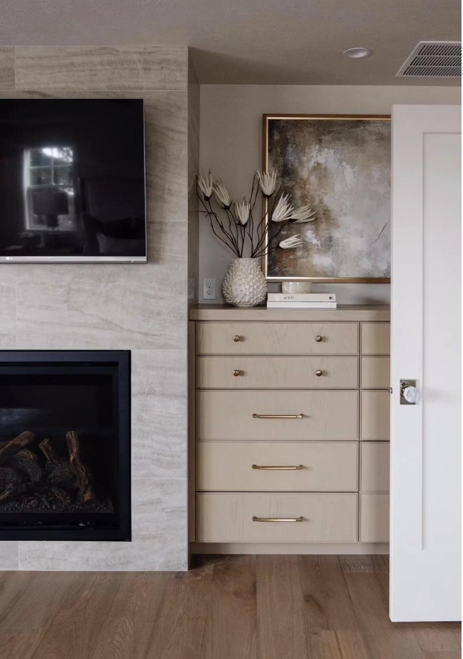 Abstract painting in warm earth tones of brown gold and cream displayed on built-in dresser in bedroom niche beside travertine fireplace surround