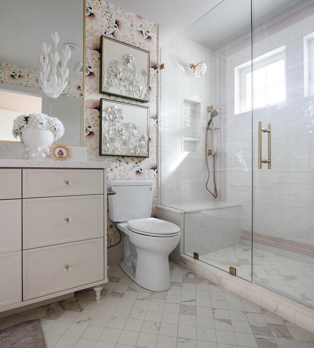 Pair of white three-dimensional floral relief sculptures in dark frames displayed in elegant bathroom with floral wallpaper glass shower and marble tile