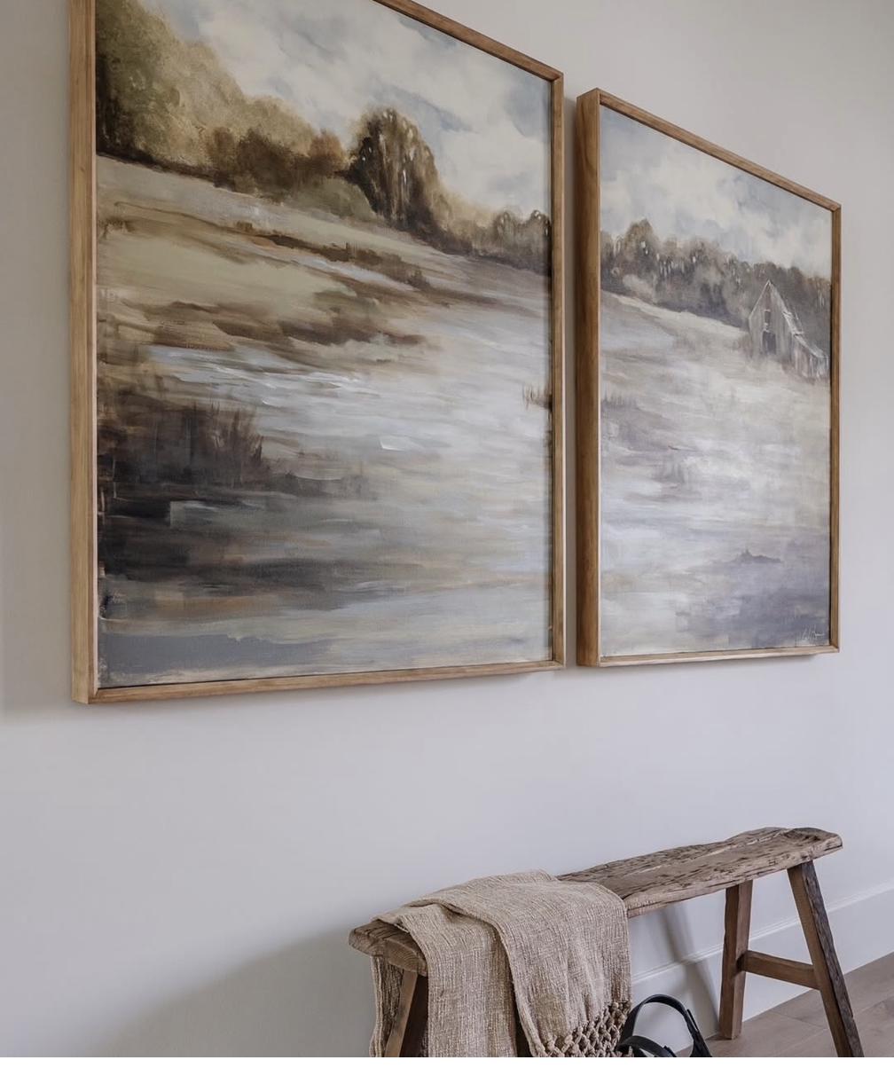 Two-panel landscape diptych painting in muted gray brown and sage tones depicting countryside with barn displayed above rustic weathered wood bench in entryway