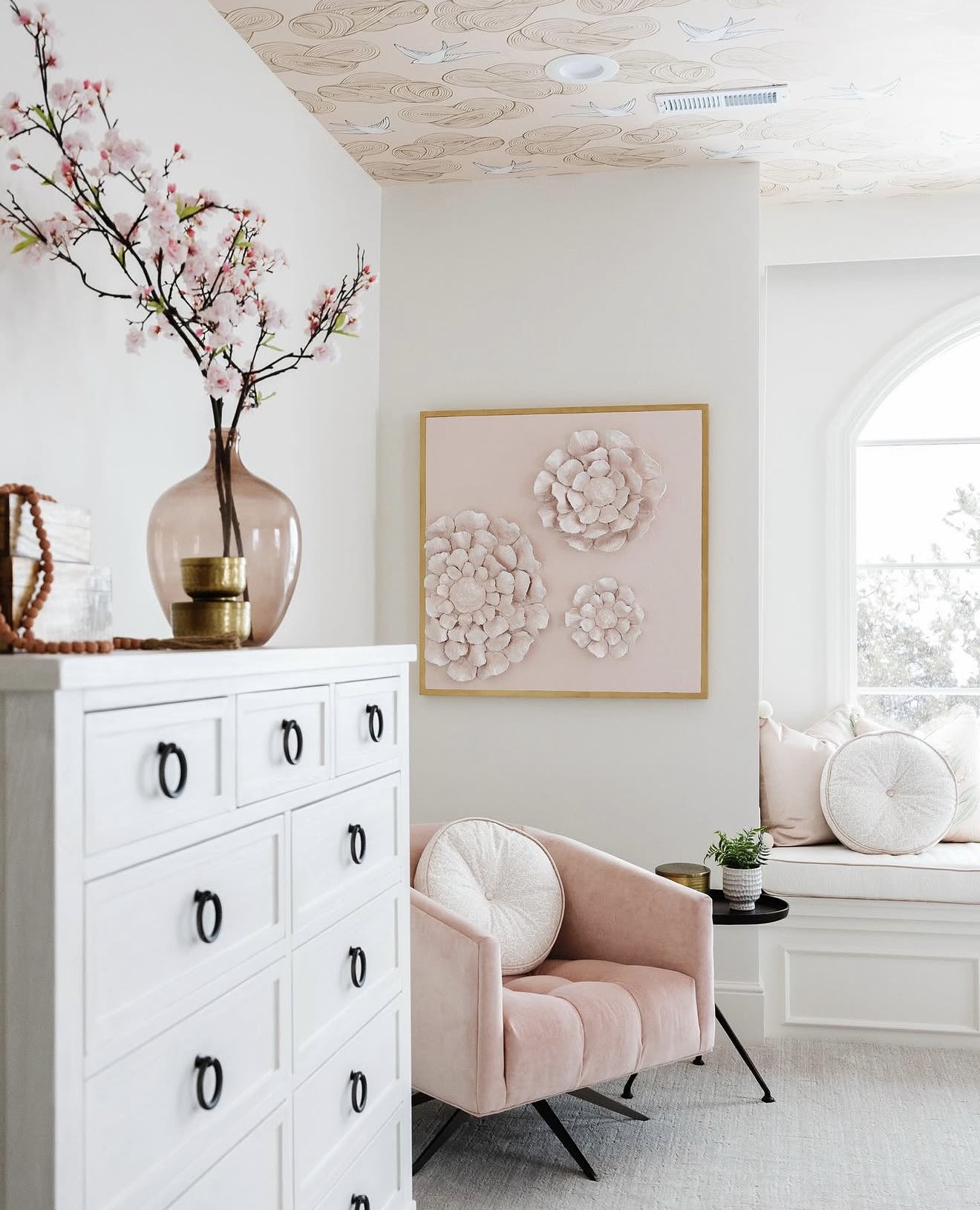 Three-dimensional floral sculptural artwork in soft pink tones displayed in elegant room with blush pink velvet chair and cherry blossom branches