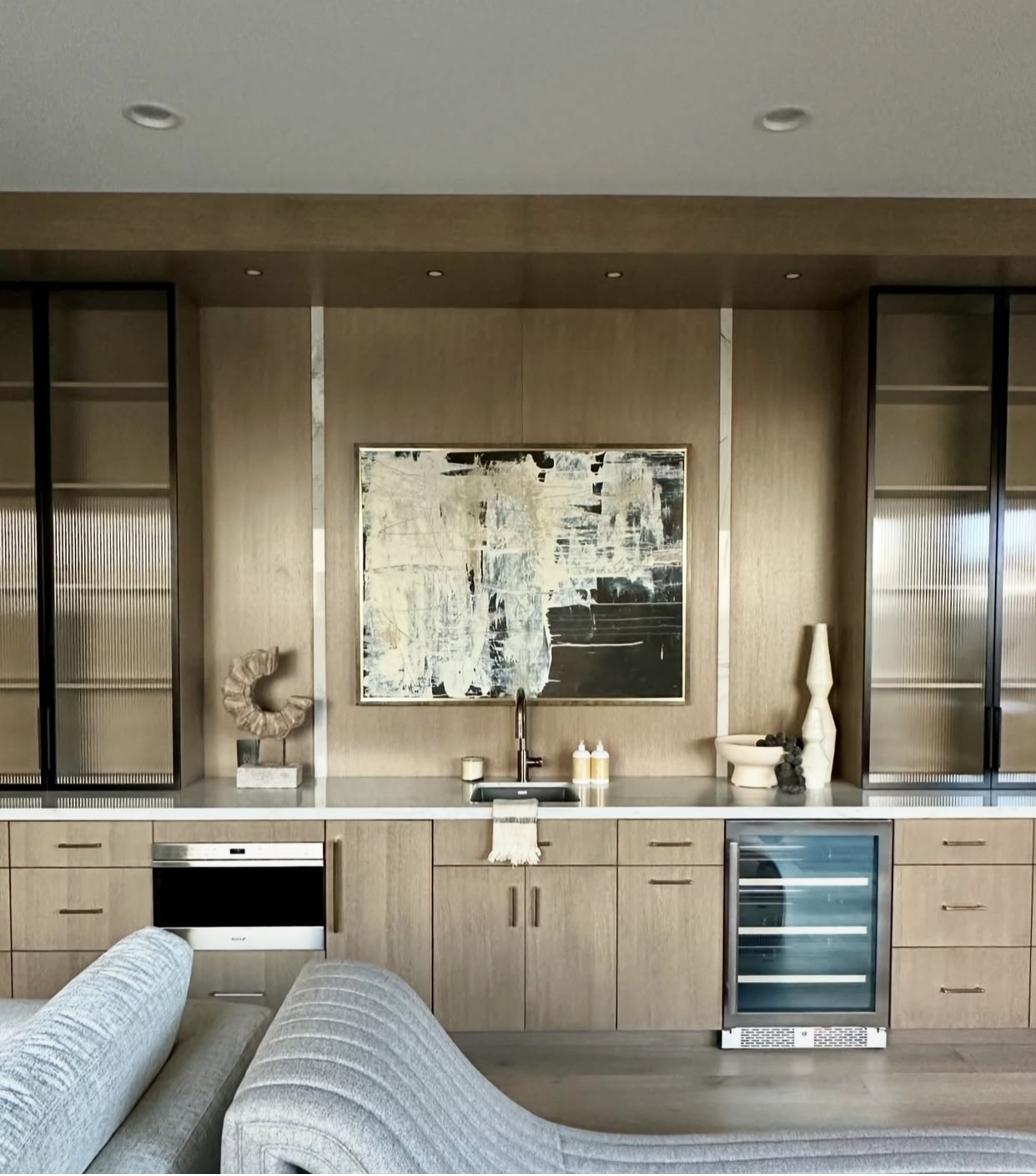 Abstract black and white painting displayed in modern kitchen bar area with fluted glass cabinets sculptural decor and wine refrigerator