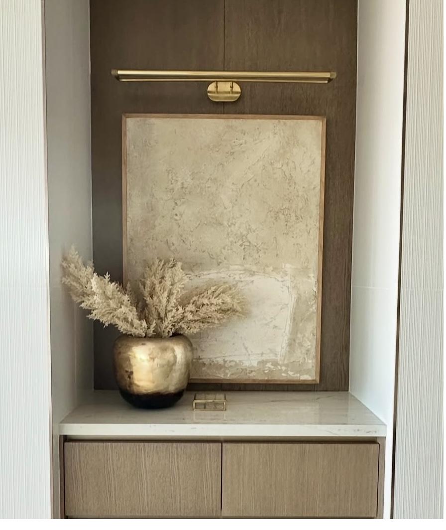 Cream and beige textured abstract painting in natural wood frame displayed in dark wood built-in niche alcove with brass picture light and gold vase with dried botanicals