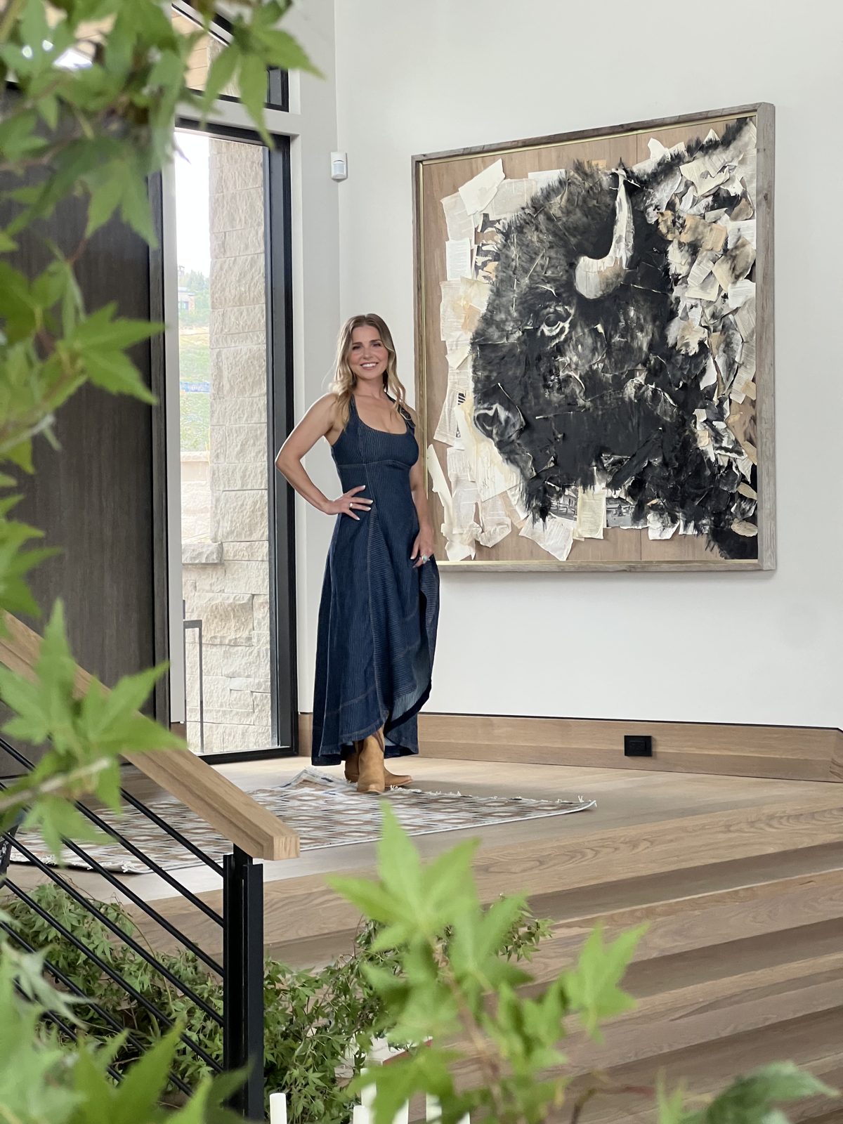 Artist Bailey Foreman standing in a bright modern home beside her large mixed media bison artwork