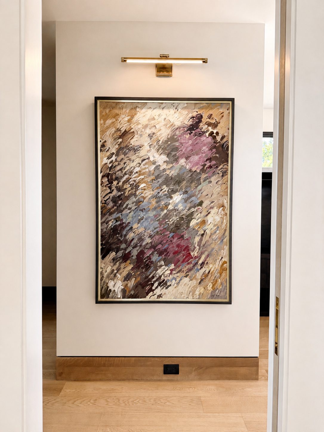 Expressive abstract painting with layered brushstrokes in mauve, dusty blue, cream, and gold lit by a brass picture light at the end of a hallway