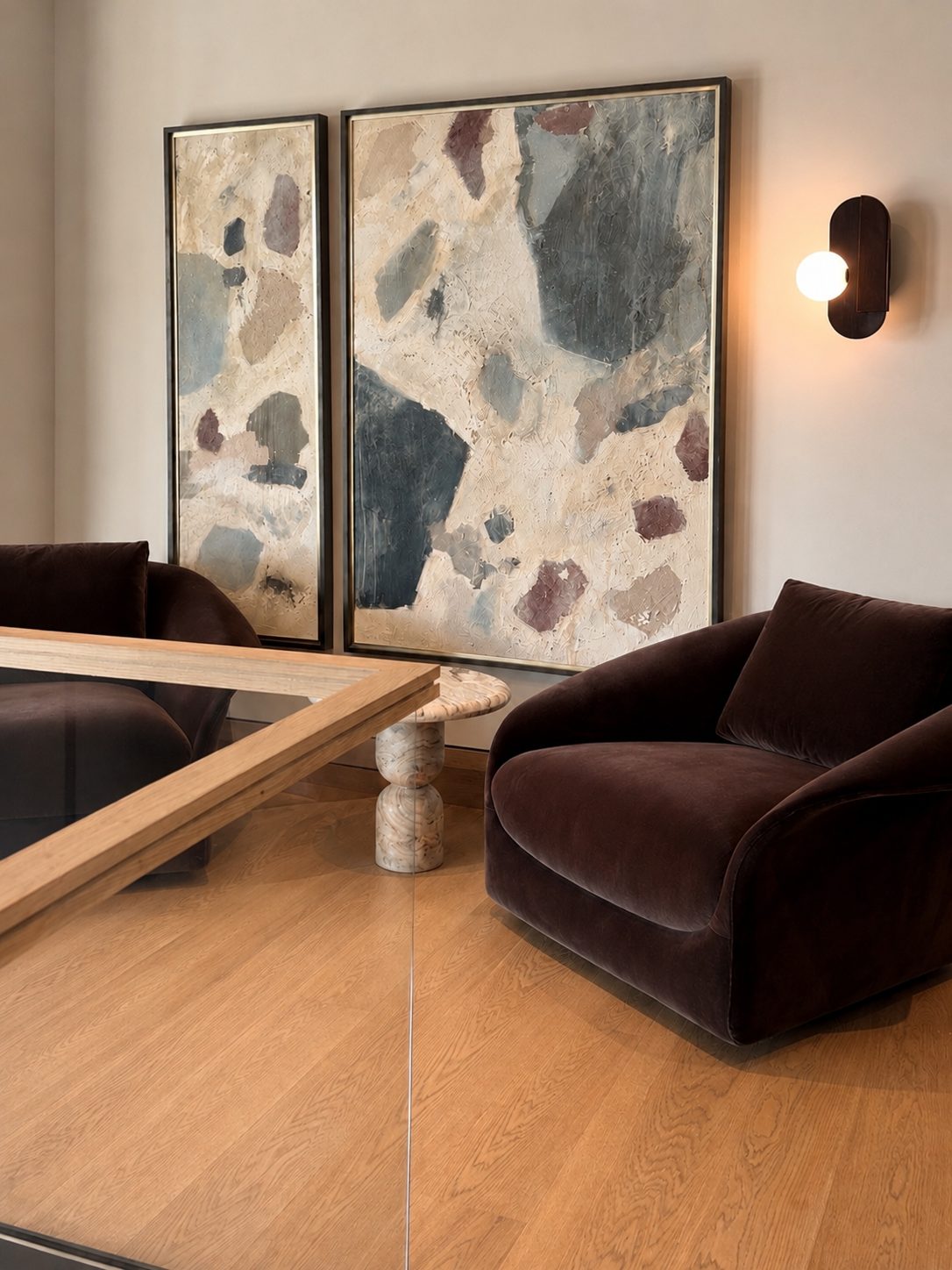 Two-panel abstract painting with organic terrazzo-like shapes in slate blue, rust, and cream hung above a living room seating area with a velvet chair